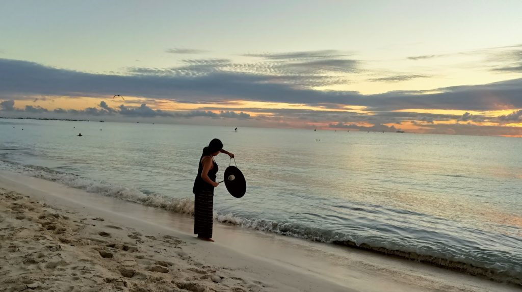 A Woman Sounds Her Gong at Dawn at Playa del Carmen